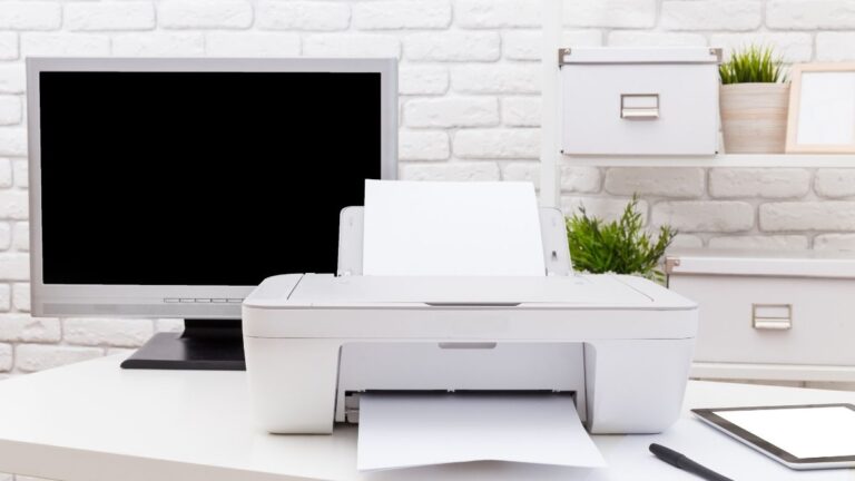impressora branca em uma mesa de escritório branca ao lado de um computador monitor